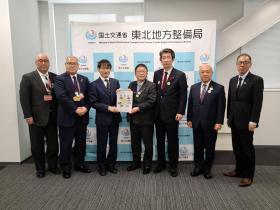 国土交通省東北地方整備局と書かれたボードの前で、市長が梅野修一局長と要望書を持っているところに同行した道路4団体の方、整備局の方も並んで7人で撮影した写真