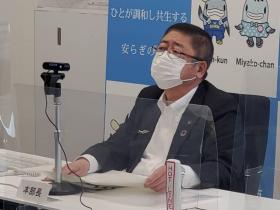アクリル版が置かれたテーブルに市長が座り意見を述べている写真