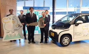 車体が白でアクセントに黒がはいったトヨタのC+pod(シーポッド)「デカボン号」と市長、関係者が記念撮影をしている写真