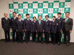 バックパネルの前で、制服姿の新規採用の消防職員7名と市長、副市長、男性1名が並んで撮影した写真