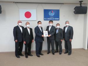 日本国旗と国土交通省 東北地方整備局の旗が壁に掲げられた会場で、スーツ姿の男性6名が並び、男性2名が中心で一緒に要望書を持って記念撮影をしている写真