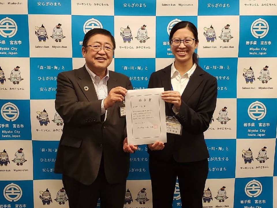 バックパネルの前で辞令書を一緒に持つ市長と宮古市地域おこし協力隊に任命された上之原良美さんの記念写真