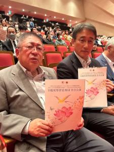 市長と副市長が講演会のポスターを持って観客席に座っている写真