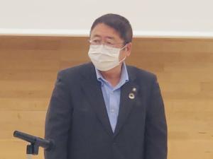 ジャケットに薄青色のシャツを着た市長がマイクスタンドの前で挨拶を行っている様子をアップで撮影した写真