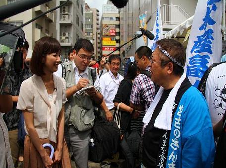 青色の半被をきた市長がアナウンサーやカメラやマイクに囲まれ取材をしている写真