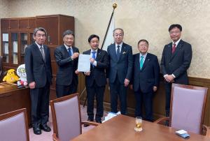 旗が設置された室内で、財務大臣政務官の瀬戸隆一氏と静岡市長の難波喬司氏が一緒に要望書を持ち、ブロック幹事の宮古市長と3名の市長が横一列に並んでいる写真