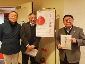 中央に市民劇のチラシが掛けられ、右側にパンフレットを持った市長、左側に関係者の男性が2名写った写真