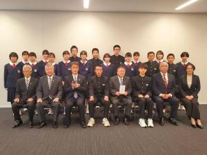 前列に学生や市長、関係者の方々8名が椅子に座り、後列に制服を着た男女の学生が立って写っている記念写真