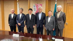 大きな茶色いテーブルを前に、市長を含めて6名のスーツを着た男性たちが並んでいる記念写真
