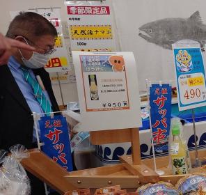 市長がサッパ市と書かれた小さい幟が立っている舟盛り用の舟に置かれている商品を見ている写真