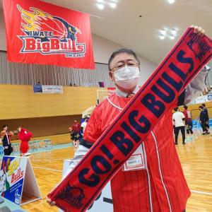 ビッグブルズの横断幕が掲げられた体育館で、「GO!BIG BULLS」と書かれたタオルを両手で持ち前方に向け斜めに広げている、赤いユニフォームを着た市長の写真