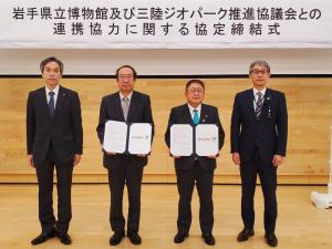 岩手県立博物館及び三陸ジオパーク推進協議会との連携協力に関する協定締結式と書かれた横断幕の下で市長と県立博物館の館長がそれぞれサインした協定書をもち、関係者2名を含めて、並んで撮影した写真