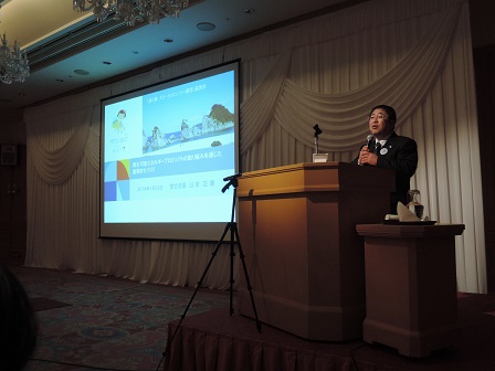 画面が映されたスクリーンの横の演台で、マイクを持ち話をする市長の写真
