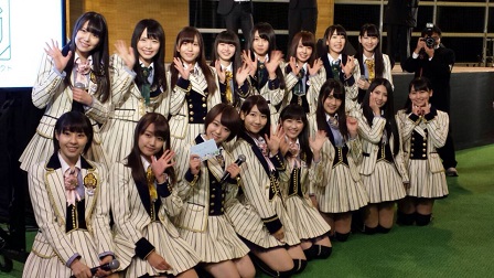 前列で8名がしゃがみ、後列で8名が立ってそれぞれポーズを決めて写るAKB48グループの方々の記念写真