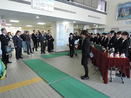 市役所のホールで並ぶ青山学院女子短期大学の関係者の方々と、向かい側に立つ市長や観客の方々の写真