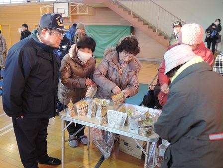 机の上に置かれたレトルト食品の封を開けている様子の参加者の方々と、机の隣で見守る市長の写真