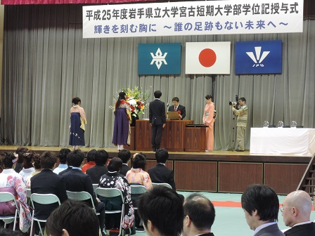 舞台上で演台越しに立つ3名の学生に向かい表彰状を読み上げる様子の市長の写真