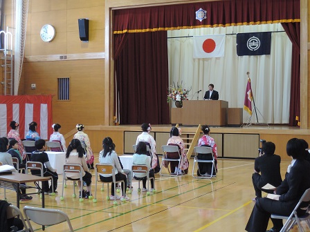 体育館に並べられた椅子に座る、袴を着た卒業生たちと、舞台上の演台のマイクに向かい話をする市長の写真