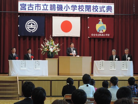 舞台上の左右に並べられたテーブルの席に着く4名の男性たちと、中央の演台に置かれたマイクに向かい話をする市長