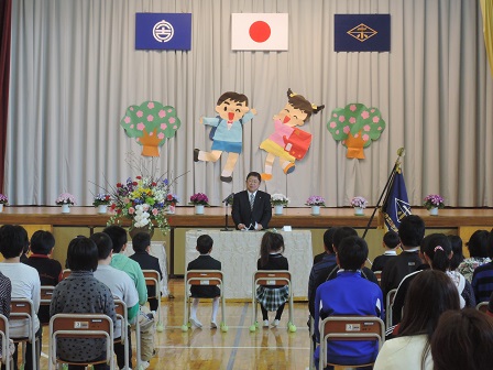 舞台の前に置かれた演台のマイクに向かい話をする市長と、椅子に座る小学生たちを写した写真