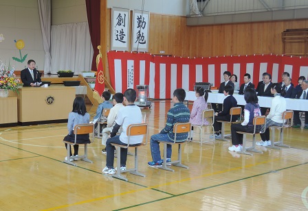 紅白幕が貼られた体育館で、椅子に座る生徒たちと、演台のマイクに向かい話をする市長の写真