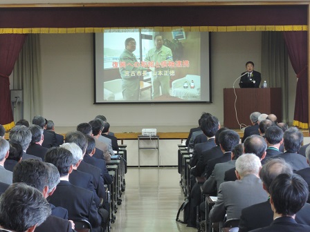 会場に並んだ机の席に座る大勢の関係者と、舞台上の演台に置かれたマイクに向かい話をする市長