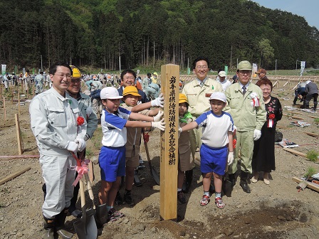 木製の記念碑を両側から支える子供たちと、周囲に立つ市長や関係者の方々の記念写真