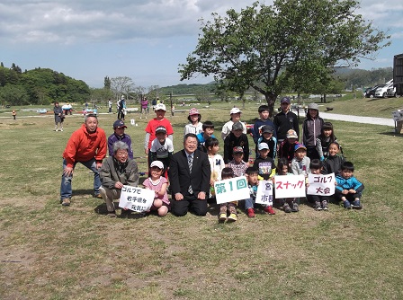 公園の芝生の上で、子供たちや関係者の方々と記念撮影をする市長の写真