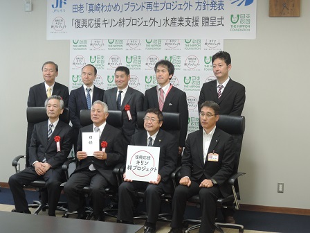 パネルを持った市長を含む男性4名が前列で椅子に座り、後列で5名の男性が立って並ぶ記念写真