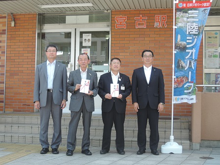 「三陸ジオパーク」と書かれたのぼり旗の隣で、目録を持つ市長と男性1名を中心に、両側に男性2名が立って並んでいる記念写真