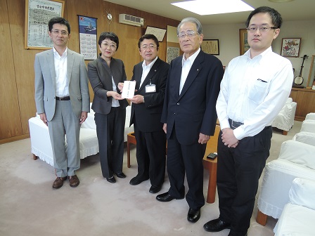 目録を一緒に持つ市長と女性、3名の男性が並んで立つ記念写真