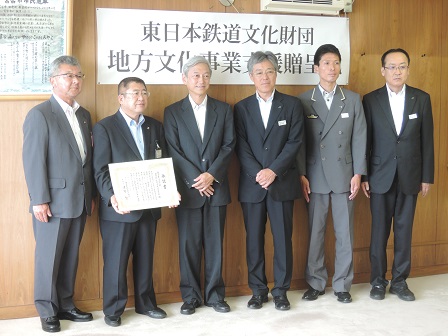 壁の前で、賞状を持つ市長と5名の男性たちが並んでいる記念写真