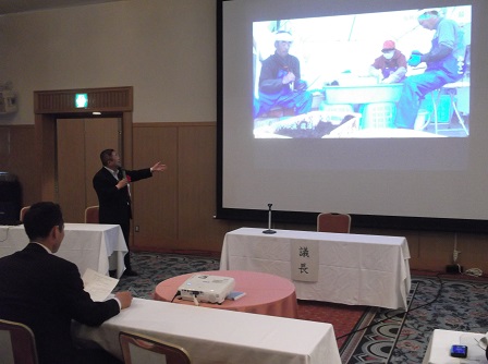 画像が映されたスクリーンの横で、右手にマイクを持ち話をしている様子の市長の写真