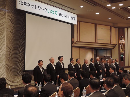 スクリーンの前に横一列に並ぶ市長と11名の男性と、向かい側で椅子に座る大勢の関係者たちを写した写真