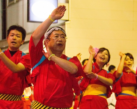 赤い浴衣を着て片手を上げて踊る様子の市長と参加者の写真