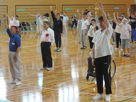 体育館で整列する市長と参加者の方々が片手を大きく上にあげている写真