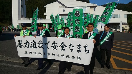 「暴力団追放で安全なまち」と書かれた横断幕と緑色の幟を持って更新する様子の市長と関係者の方々の写真