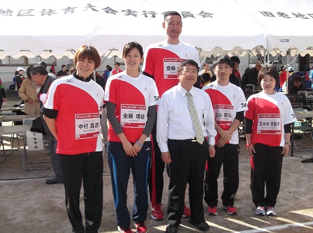 市長と、赤色と白色のTシャツを着た5名の選手が並んでいる記念写真