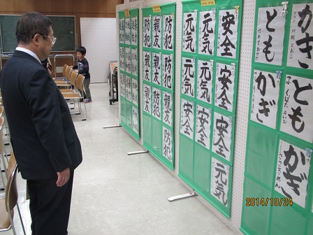 「安全」「元気」などの文字が書かれた習字紙が貼られたボードの前に立ち観覧している様子の市長の写真