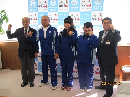 ジャージを着た3名の選手と市長、関係者の男性が握った拳を顔の横に掲げてポーズをとっている記念写真