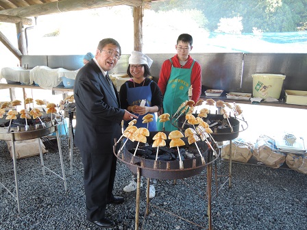 炭の周りに並べて刺された串焼きと市長、子供2名が写っている写真