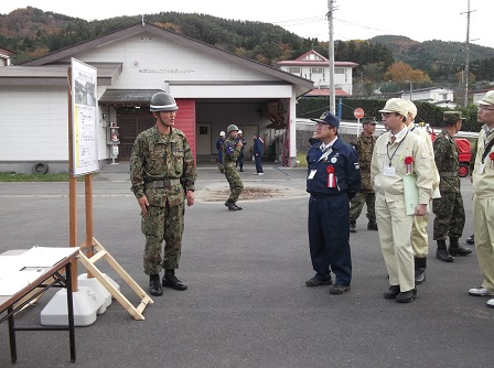 迷彩服を着てヘルメットを被った自衛隊員の向かい側に立つ、市長と関係者たちの写真
