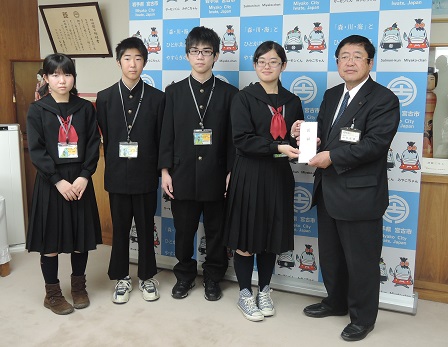 バックパネルの前で目録を一緒に持つ市長と女子中学生の隣に、男子中学生2名と女子中学生1名が並んで立つ記念写真