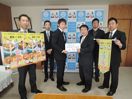 ポスターとフラッグを持つ男性2名、「義援金」と書かれた箱を一緒に持つ男性と市長、バックパネルの前で左右に分かれて立つ男性2名の記念写真