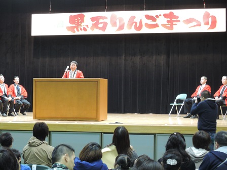 「黒石りんごまつり」と書かれた横断幕が吊るされた舞台で、演台のマイクに向かい話をする市長の写真