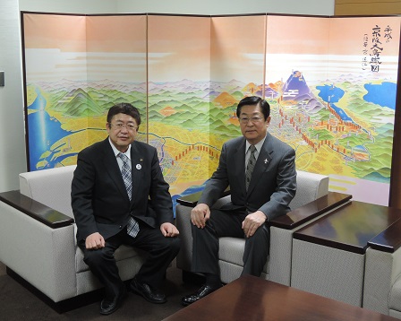 加藤好文社長と山本市長が京都の風景が描かれた屏風の前に座っている写真
