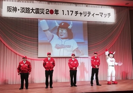 チームのキャラクターのバッファローマンがスクリーンに映し出された ステージ上で、赤の帽子、赤のジャンパー姿の山本市長と他3人、バッファローマンが 並んでいる写真