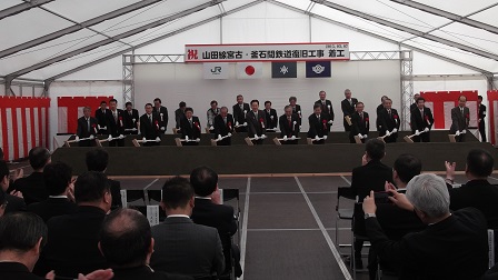 祝山田線宮古・釜石間の鉄道復旧工事着工と書かれた横断幕の下で、多くの関係者が座って見ている前で、市長を含めた20人ほどで鍬入れを行っている写真