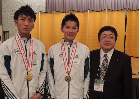 大学のウインドブレーカー姿で箱根駅伝優勝のメダルを各々かけた渡邊利典さんと他の選手1人が市長と金屛風の前で、並んで撮影した写真