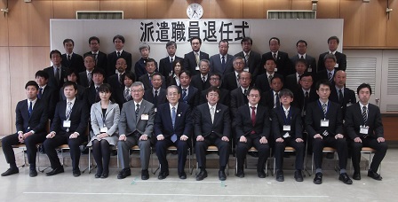 派遣職員退任式と書かれた横断幕の下で、退任される派遣職員の方々が市長を中心にして4列に並んで撮影した写真